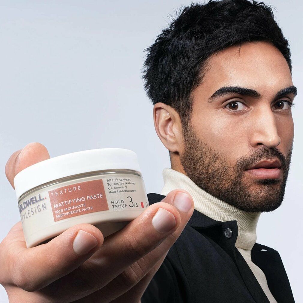 Mann hält Goldwell Stylesign Texture Mattierende Paste. Beige Dose mit weißem Deckel. Produktname sichtbar.