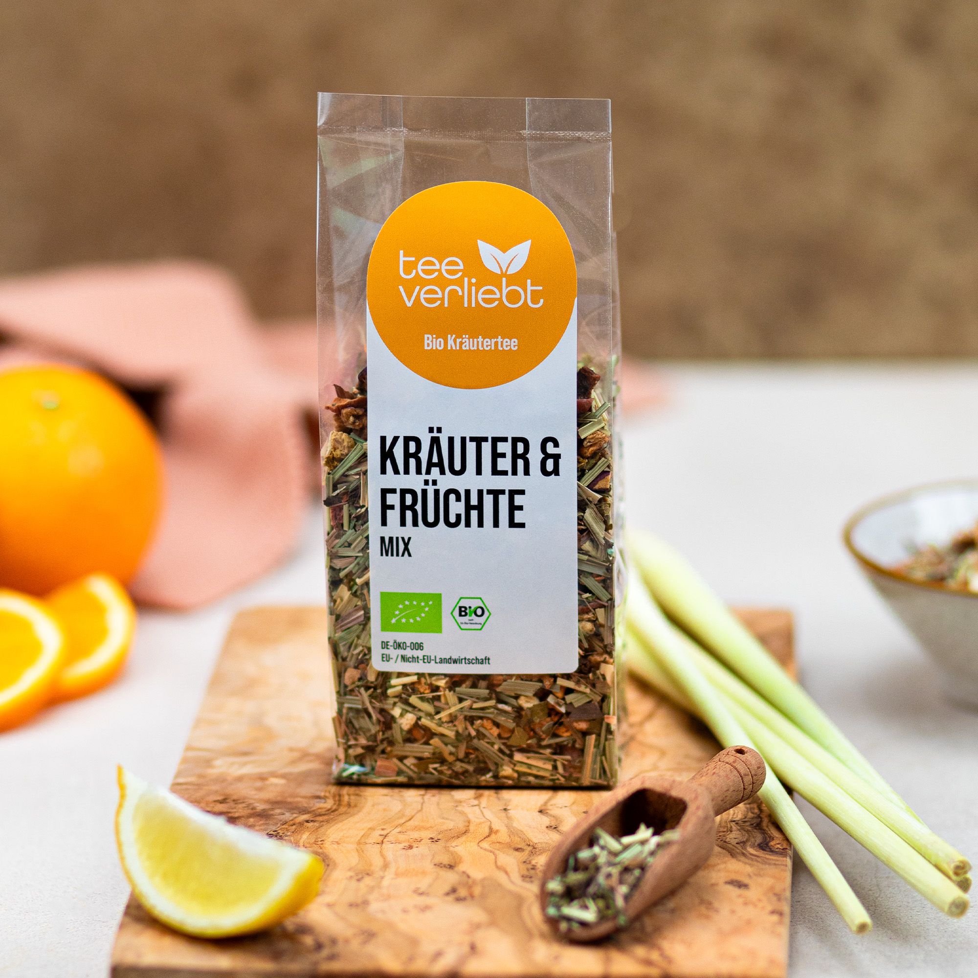 Verpackung mit Kräuter- und Früchtemischung auf Holzbrett. Orange, Zitrone, Zitronengras und Holzlöffel mit Tee. Bio-Siegel.