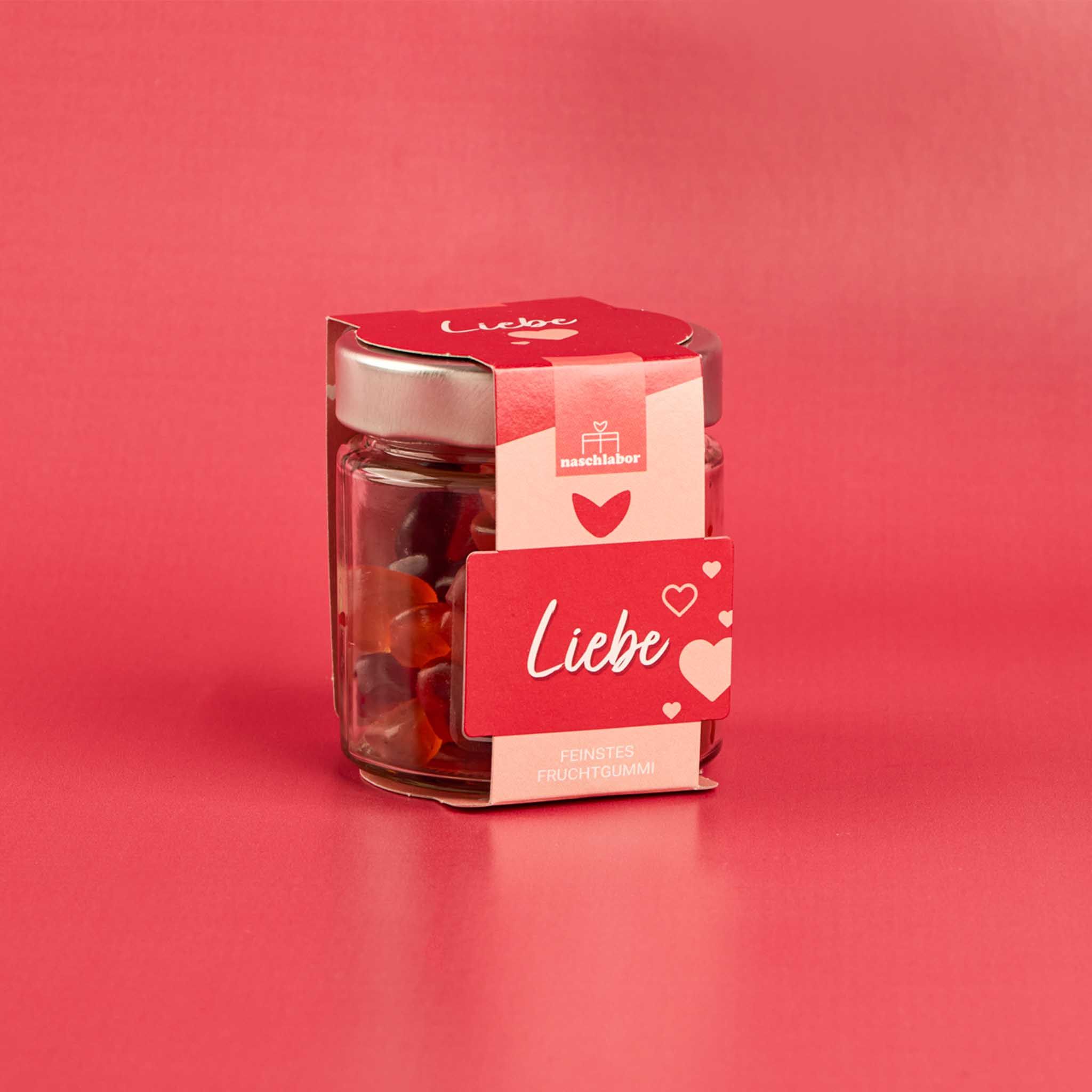 Glas mit Fruchtgummi. Roter Aufkleber mit "Liebe" und Herz-Motiven. Hintergrund rot.