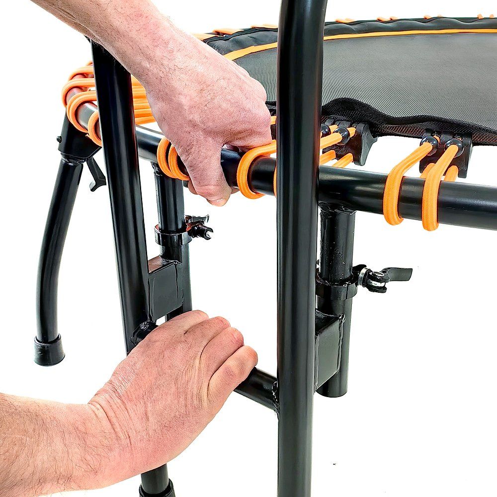 Hände montieren Haltegriff an Trampolin. Schwarzer Rahmen, orangefarbene Elemente. Nahaufnahme.