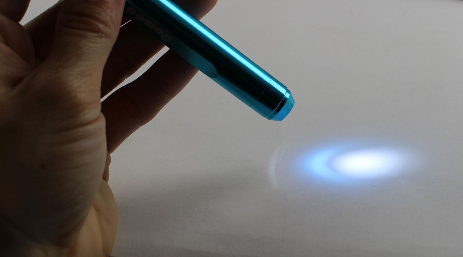 Hand hält blaue Romed Diagnostikleuchte Penlight deLuxe, Lichtstrahl auf Oberfläche.
