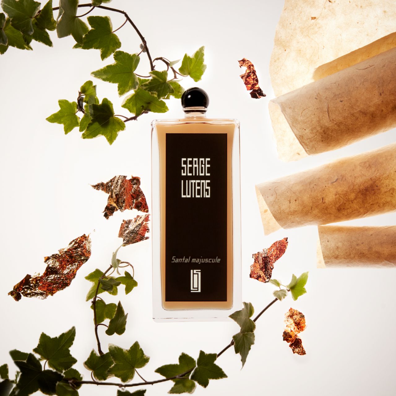 Flakon mit Blättern und Papier. Aufschrift: SERGE LUTENS, Santal Majuscule. Schwarzer Verschluss.