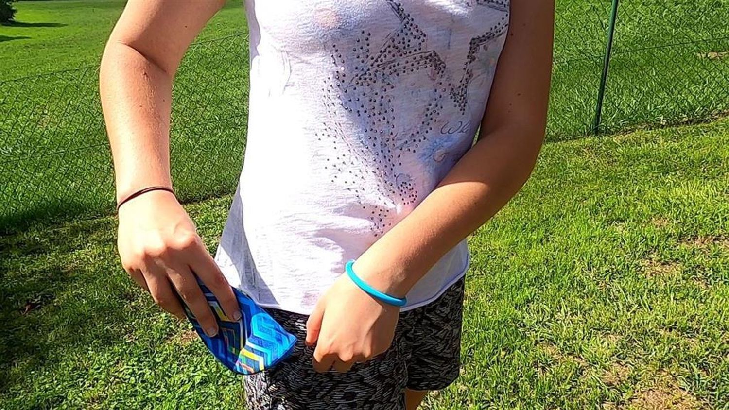 Person hält blaue Wurfscheibe. Helle Kleidung, Armband.