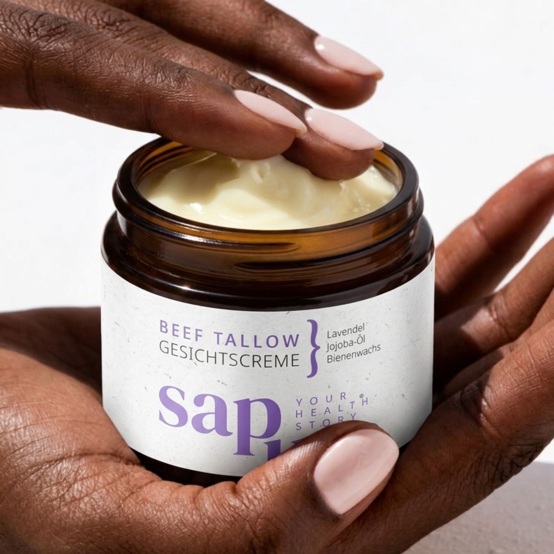 Hände halten Creme-Glas. Aufschrift: BEEF TALLOW GESICHTSCREME, Lavendel, Jojoba-Öl, Bienenwachs. Marke: sapura. Creme sichtbar.