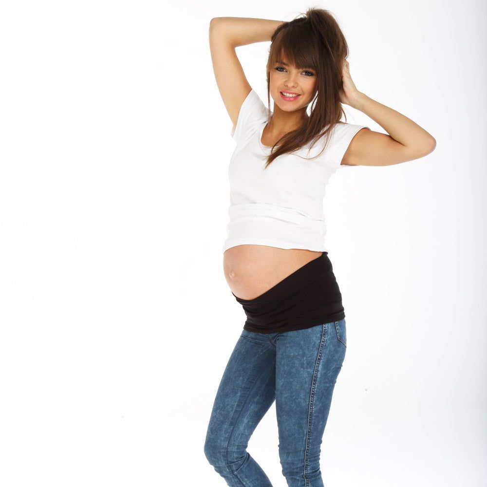 Schwarzes Bauchband, getragen von einer Frau in Jeans und weißem T-Shirt. Das Band bedeckt den Bauch.