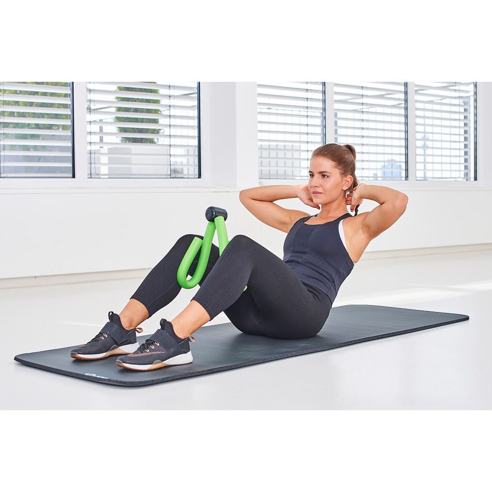 Frau macht Crunches mit dem grünen Bein-Trainer zwischen den Knien.