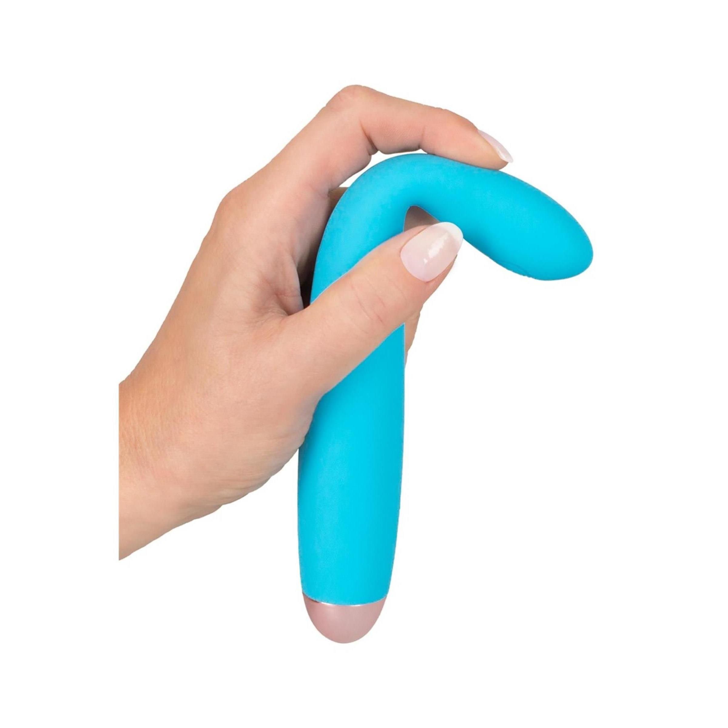 Hand hält türkisfarbenen Vibrator mit goldfarbener Spitze. Auf weißem Hintergrund.