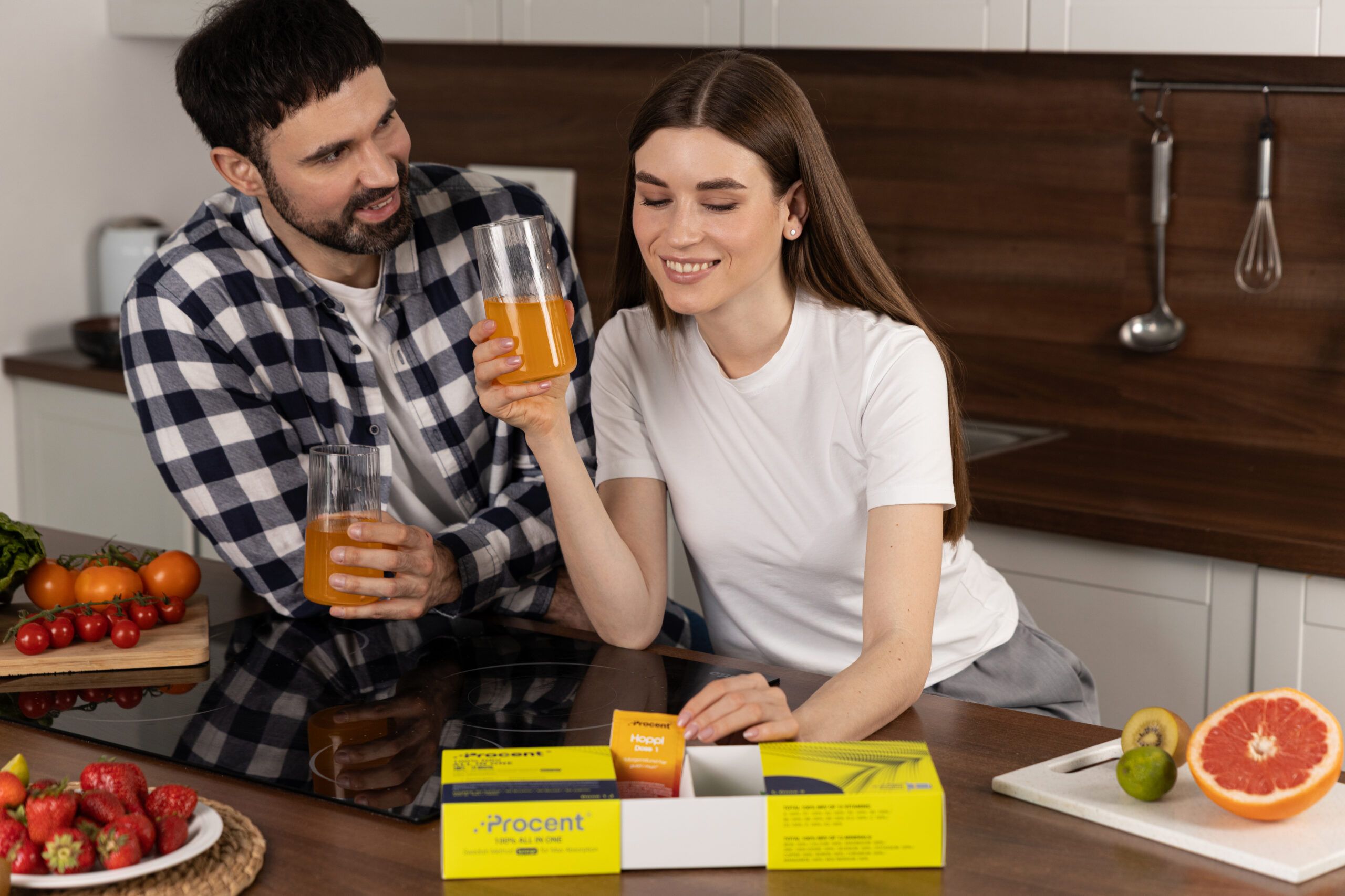 Paar mit Getränken und PROCENT-Box. Auf dem Tisch: Obst, PROCENT-Box, Gläser.